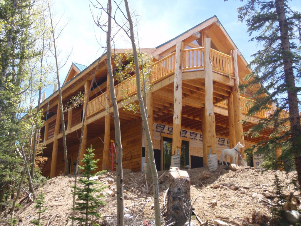 Two-story natural oak cabin under construction beside mature trees