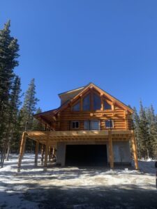 Log cabin under construction with wooden deck and oversized garage