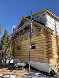 Two-story log cabin under construction with metal support beams