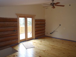 Room with wood flooring and large planks partially covering sheetrock