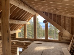 Log cabin under construction with large windows and partially-built loft