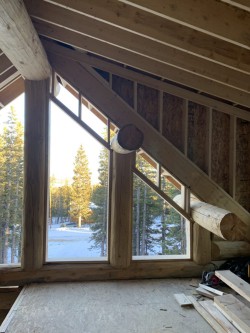 Partially-constructed loft in multistory log cabin with windows overlooking forest