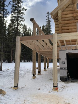 Framework for wooden deck beside partially-built log cabin