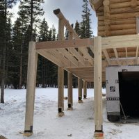 Framework for wooden deck beside partially-built log cabin