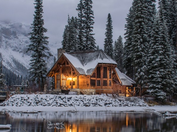 Log cabin beside mountains, lake and snow-covered pine trees